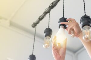 Hand screwing in lightbulb in a set of four hanging light pendants